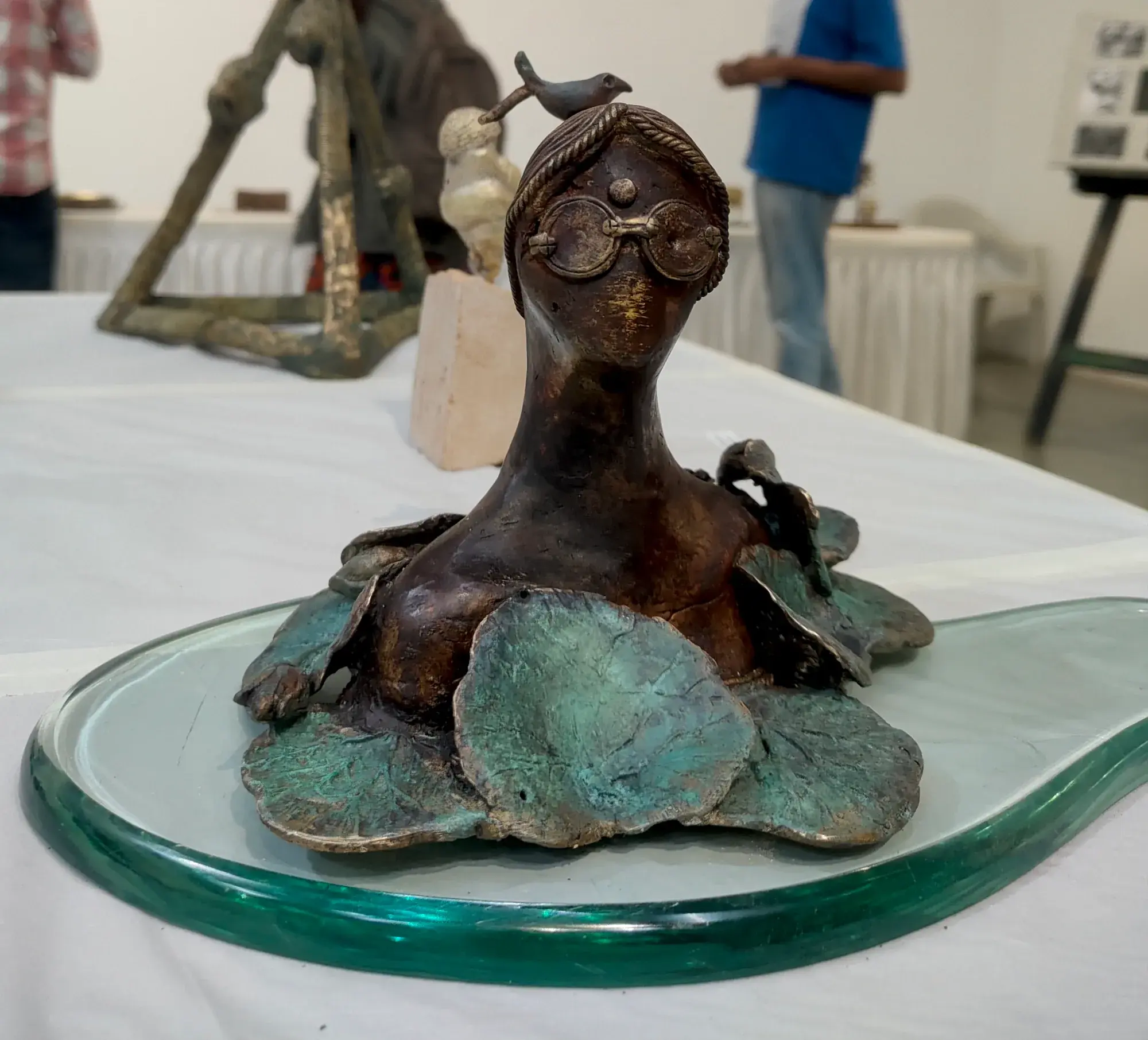 Gazing in My Lily Pond — a small bronze figure with a bird on its head, seated amid bronze lily pads on a glass base