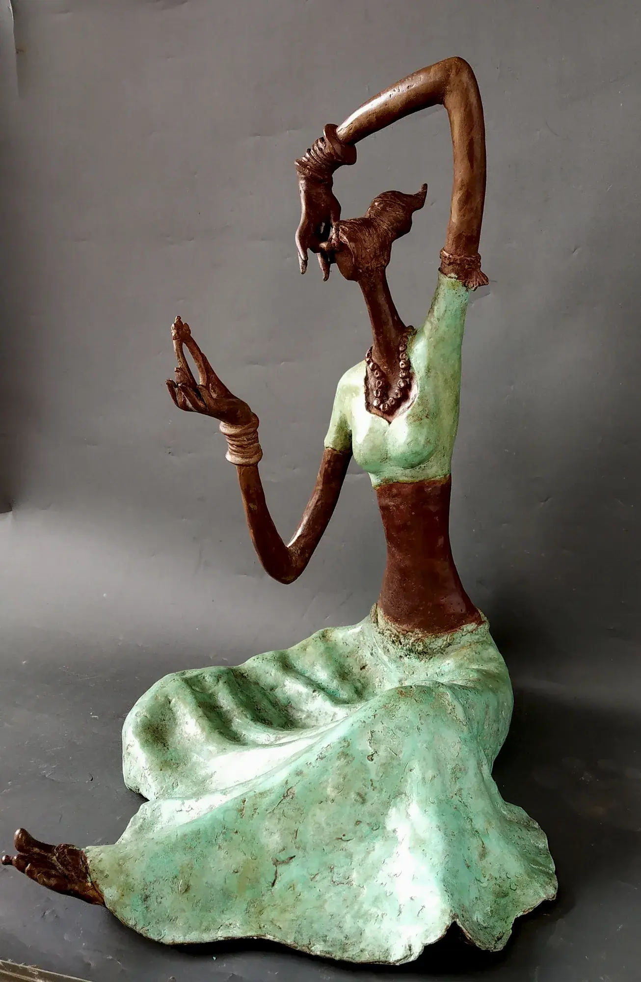 Lady with a Mirror III — bronze seated figure in mint-green patina dress, one arm arced overhead holding a small mirror