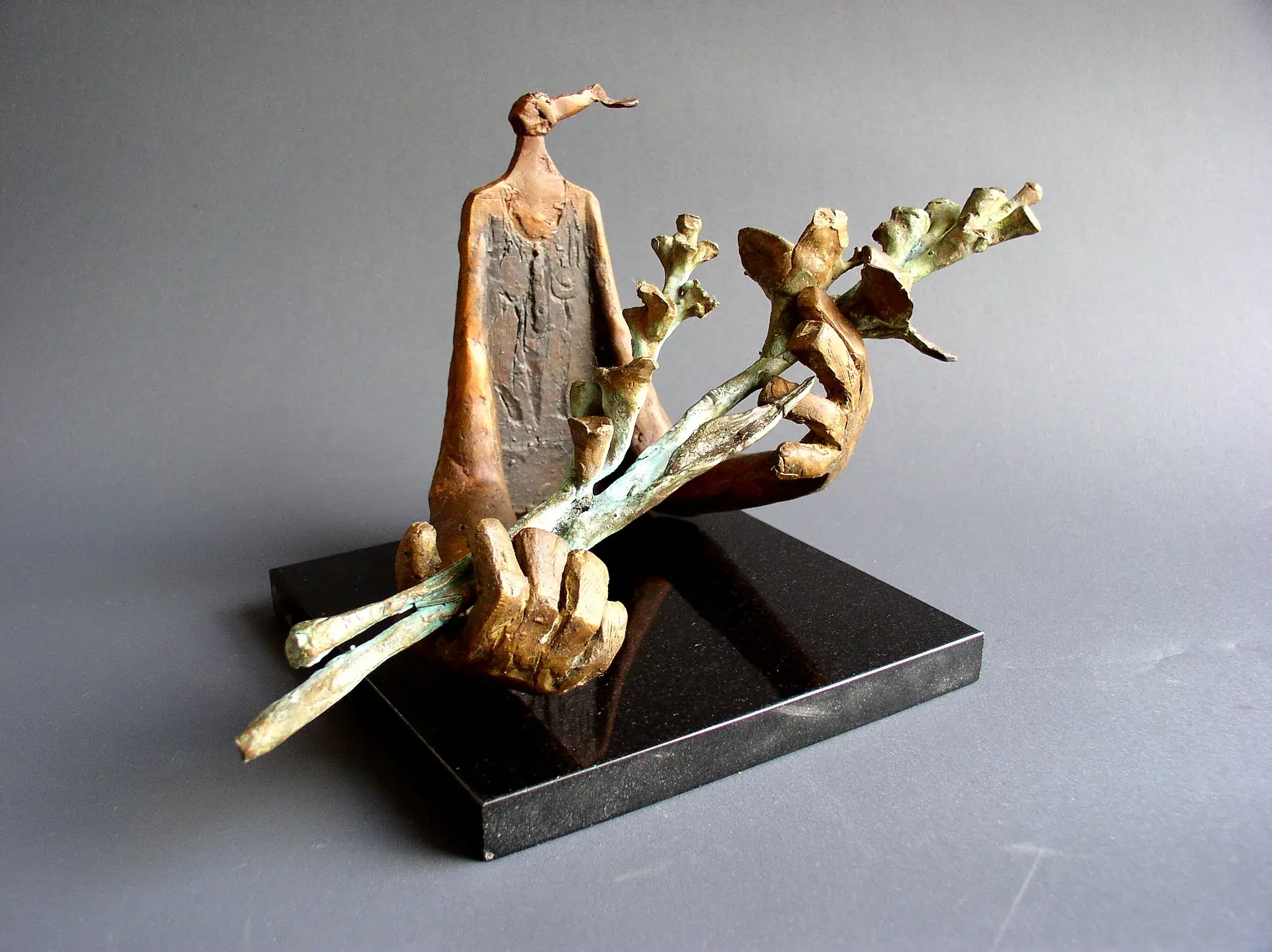 A robed bronze figure holding budding branches, mounted on a black base
